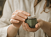 A person in a light shirt gently opens a small green jar, focusing on its contents.