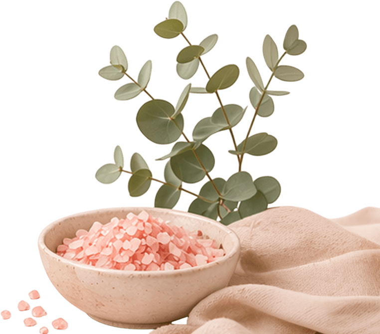 A bowl of pink Himalayan salt on a beige cloth, with eucalyptus leaves in the background against a black backdrop, creating a calm, natural setting.